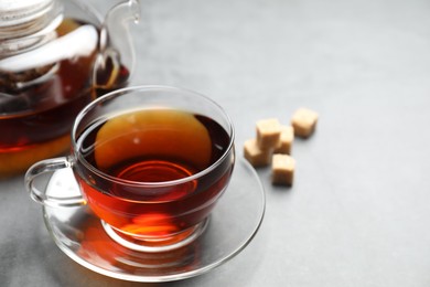 Photo of Aromatic black tea and brown sugar cubes on light grey table, closeup. Space for text