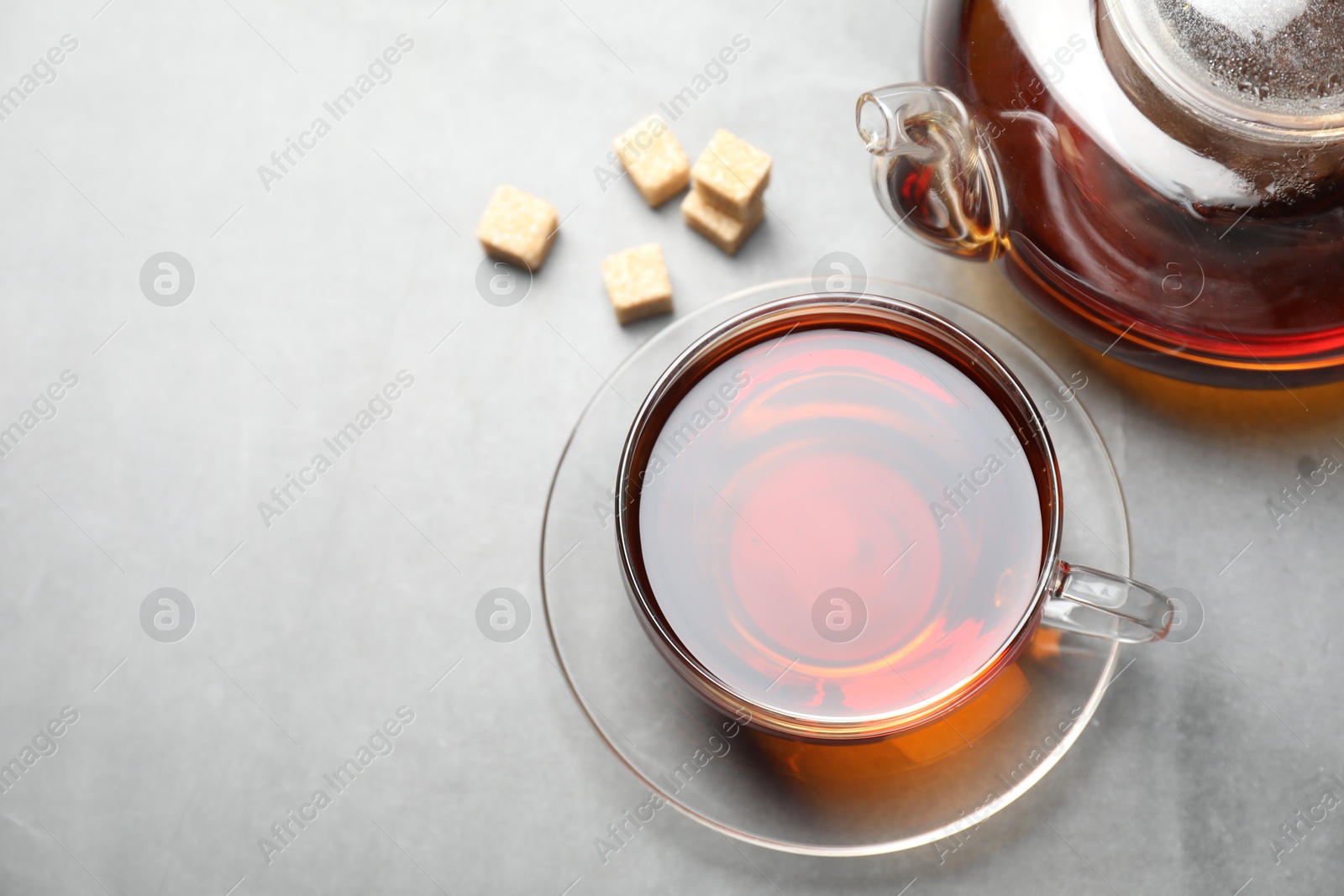 Photo of Aromatic black tea and brown sugar cubes on light grey table, above view. Space for text