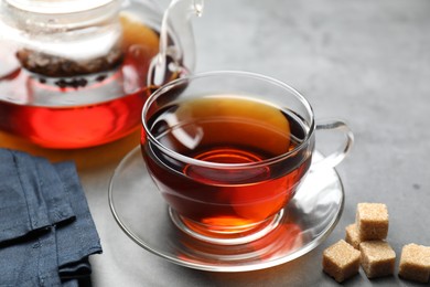 Photo of Aromatic black tea and brown sugar cubes on light grey table, closeup