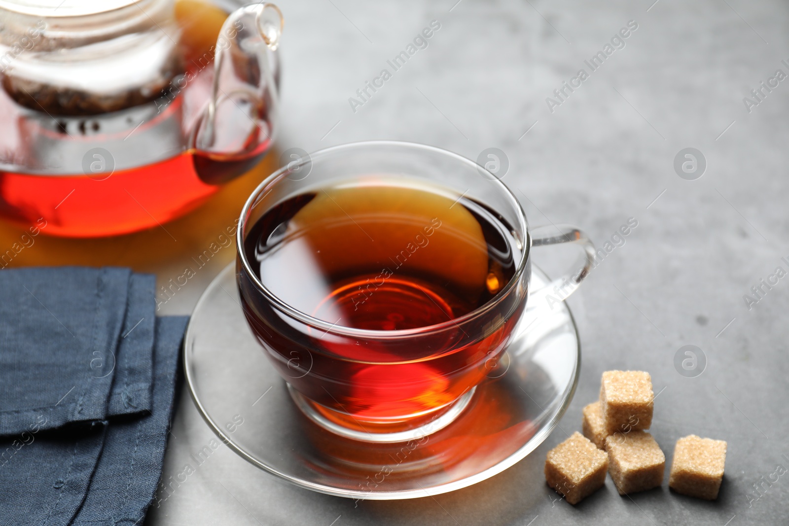 Photo of Aromatic black tea and brown sugar cubes on light grey table, closeup