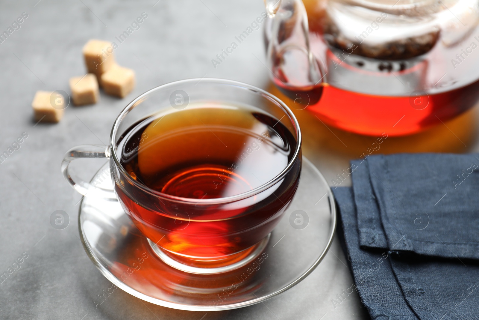 Photo of Aromatic black tea and brown sugar cubes on light grey table, closeup