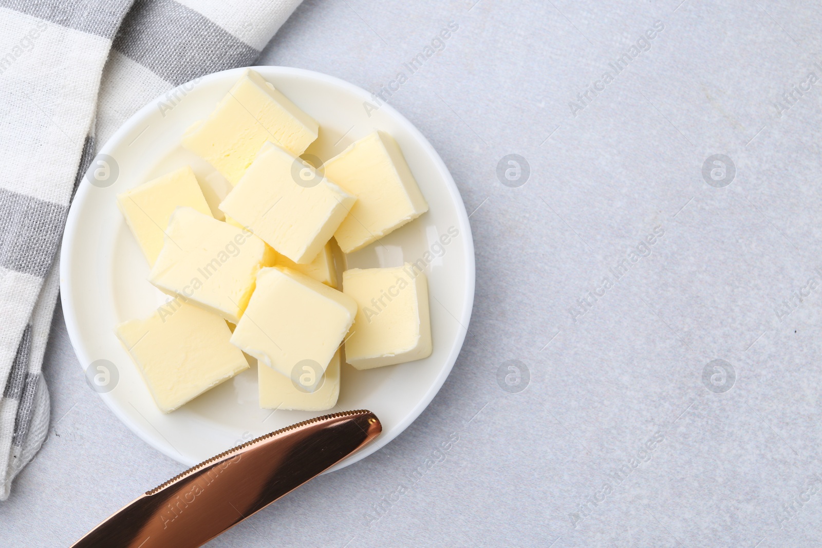 Photo of Pieces of fresh butter and knife on white table, top view. Space for text