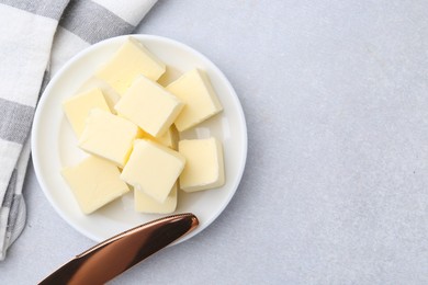 Photo of Pieces of fresh butter and knife on white table, top view. Space for text