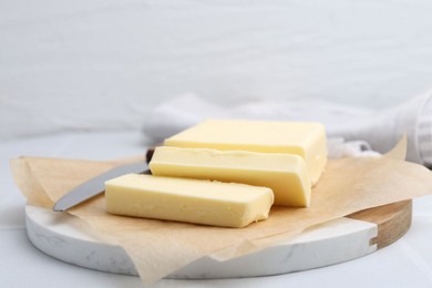 Photo of Cut block of fresh butter and knife on white table, closeup