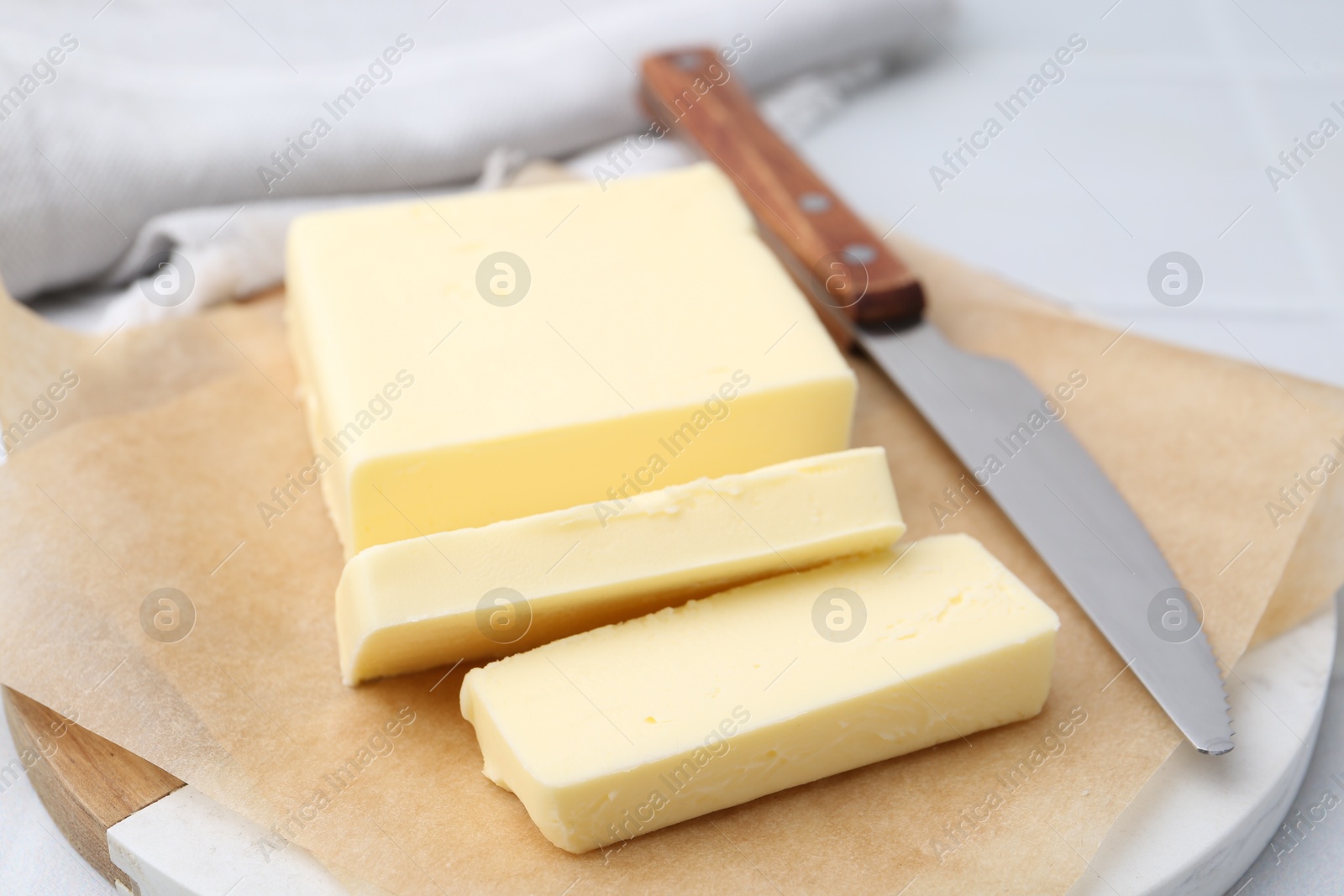 Photo of Cut block of fresh butter and knife on white table, closeup