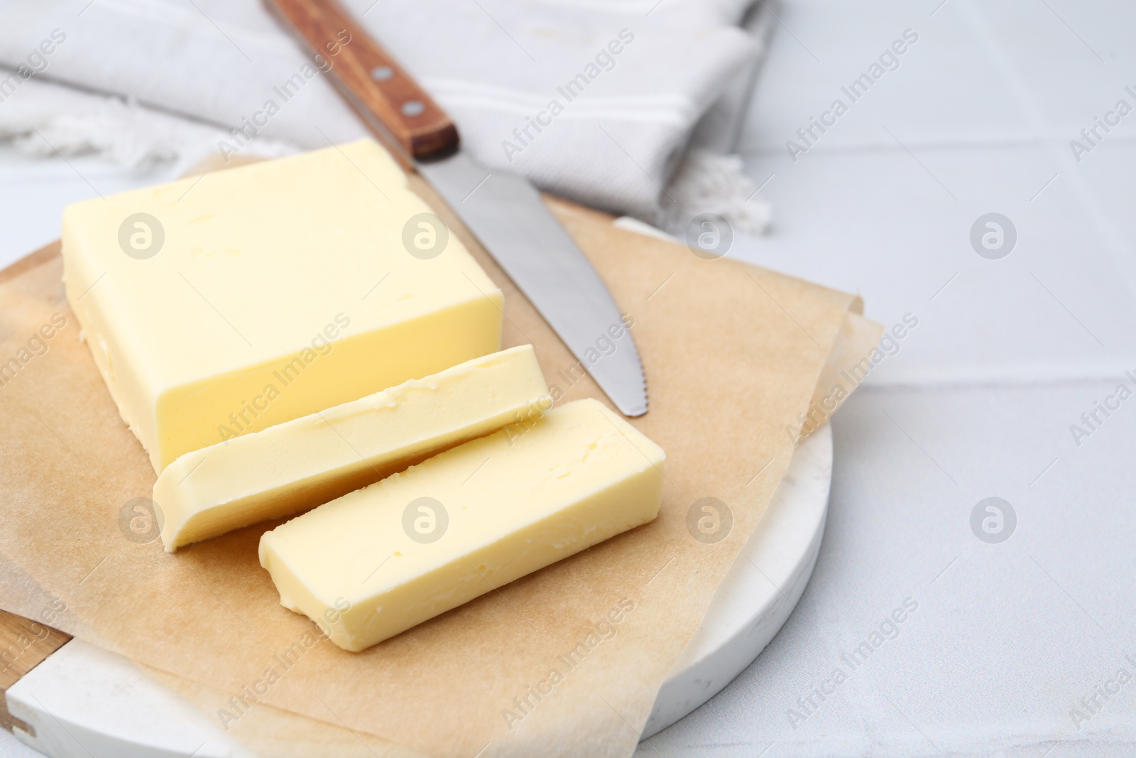 Photo of Cut block of fresh butter and knife on white tiled table, closeup. Space for text