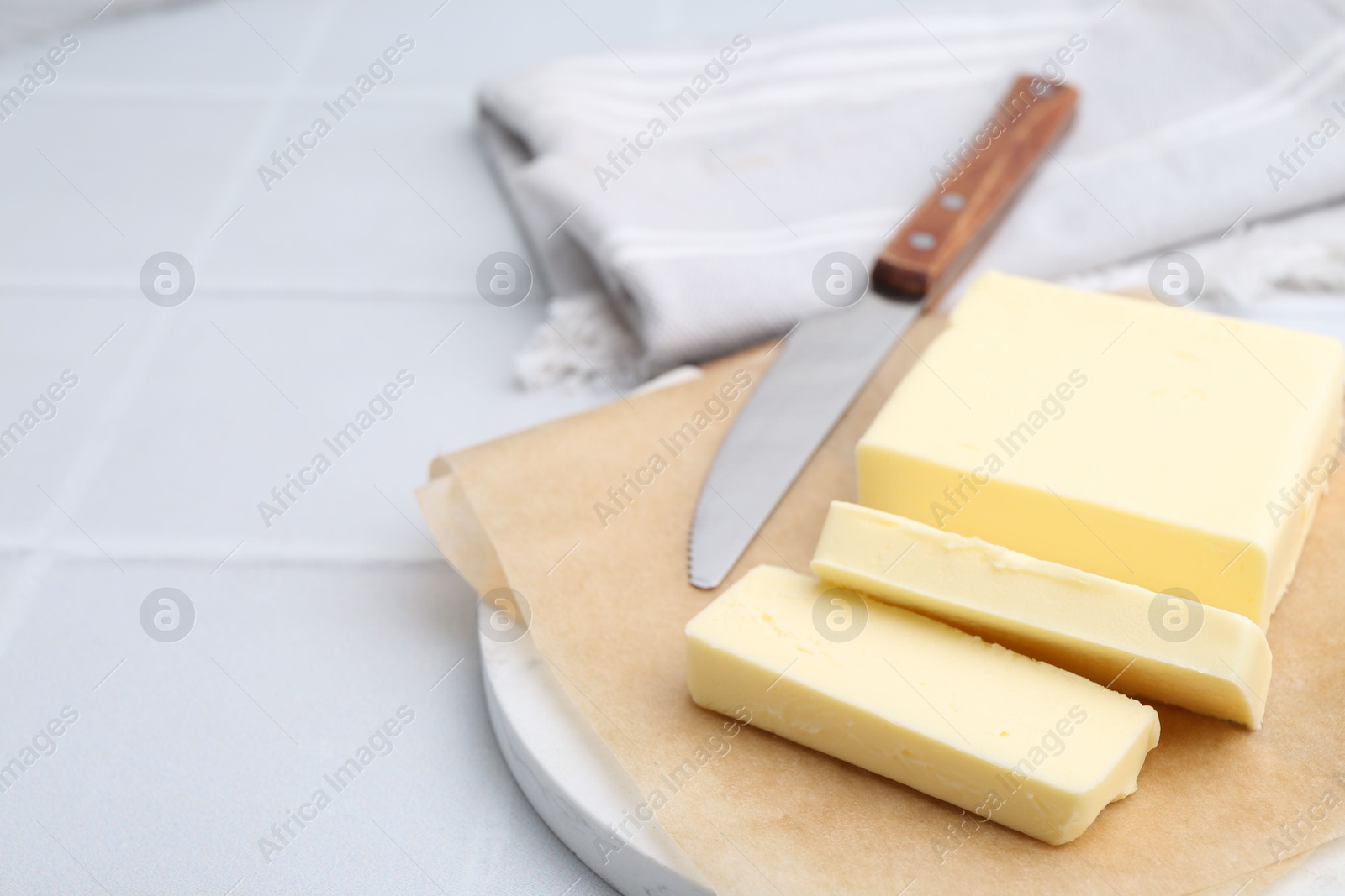 Photo of Cut block of fresh butter and knife on white tiled table, closeup. Space for text