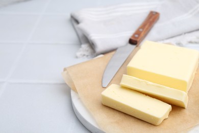 Cut block of fresh butter and knife on white tiled table, closeup. Space for text