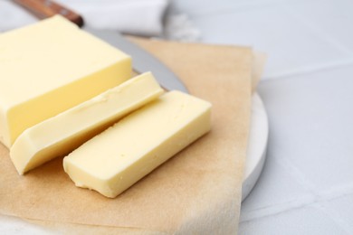 Photo of Cut block of fresh butter and knife on white tiled table, closeup