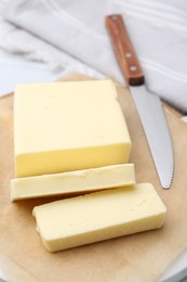 Photo of Cut block of fresh butter and knife on white table, closeup