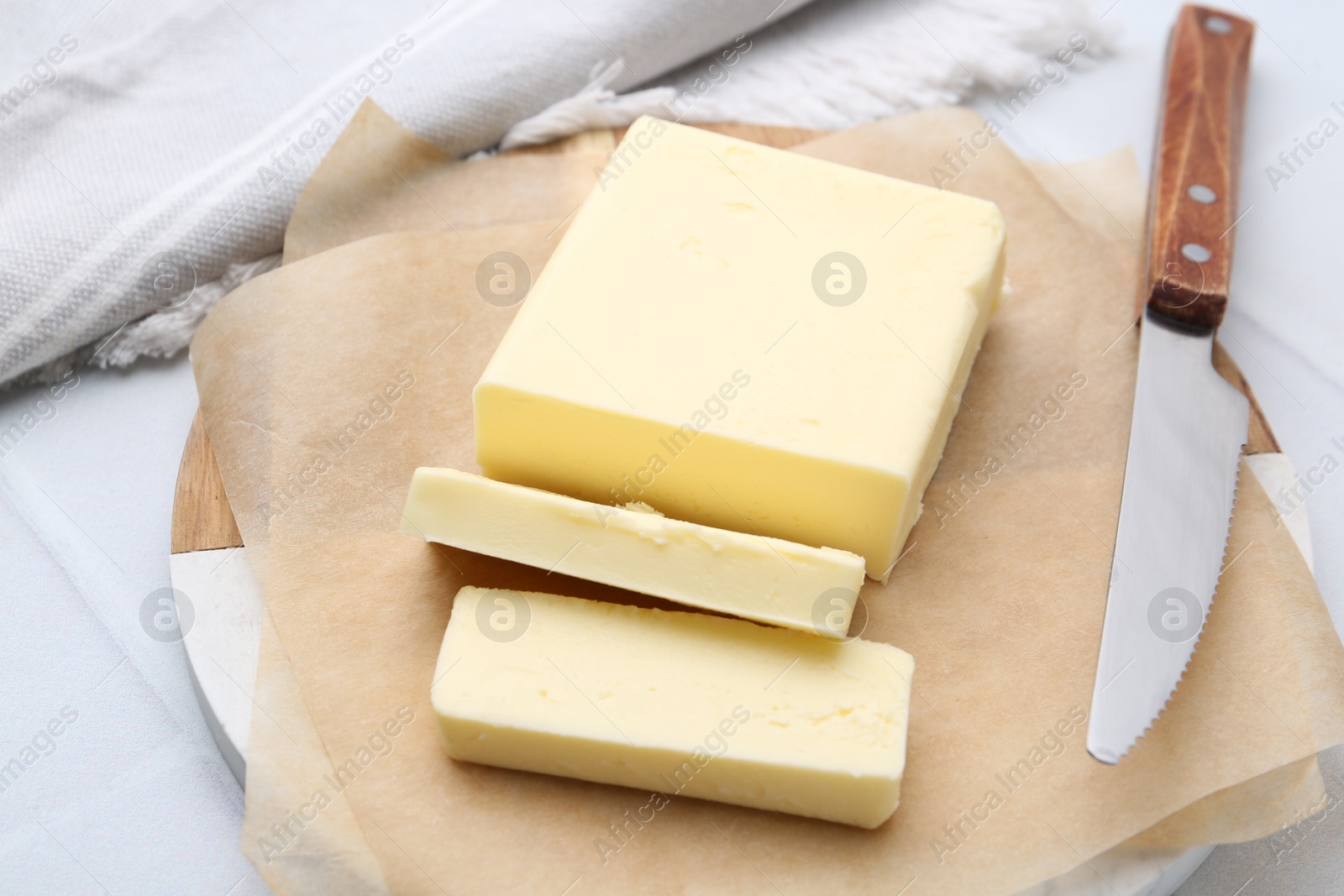 Photo of Cut block of fresh butter and knife on white tiled table, closeup