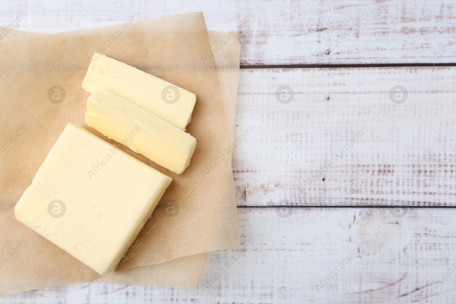 Photo of Cut block of fresh butter on white wooden table, top view. Space for text