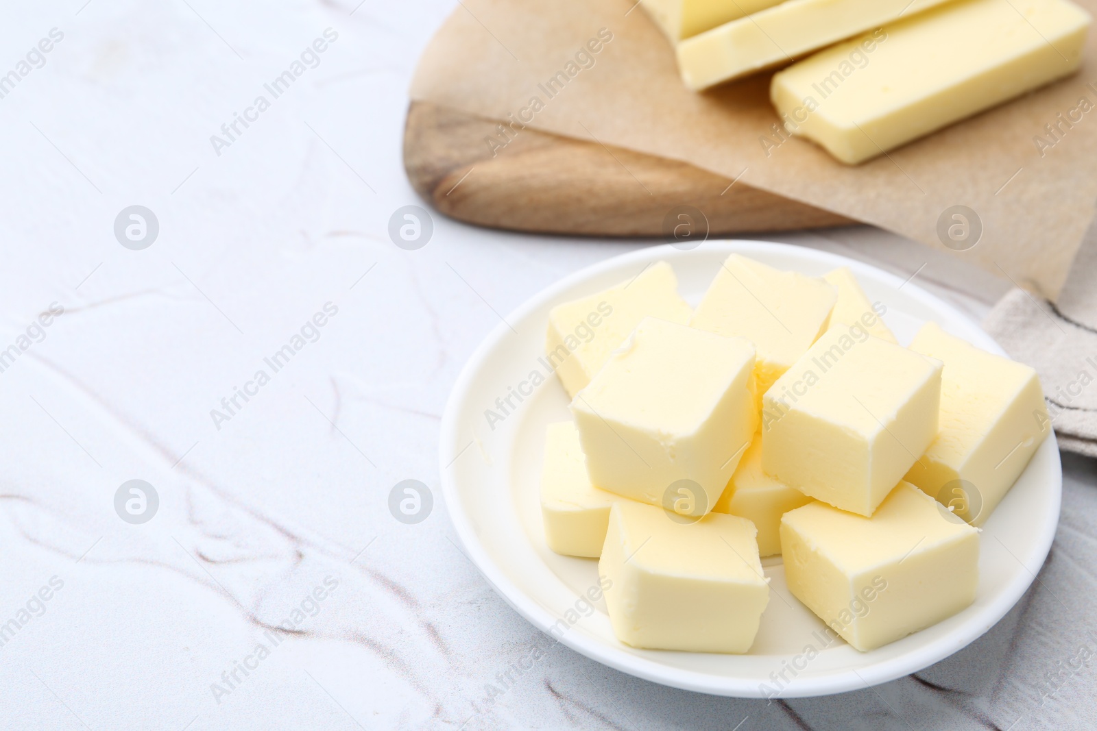 Photo of Pieces of fresh butter on white textured table, closeup. Space for text