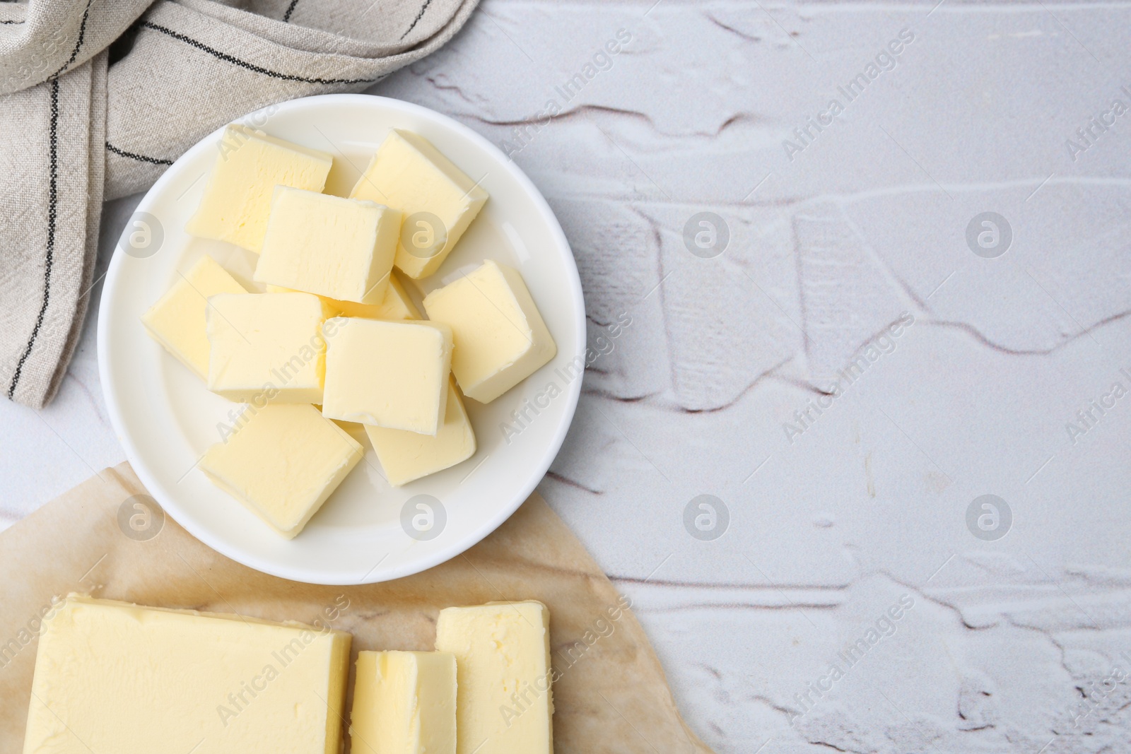 Photo of Pieces of fresh butter on white textured table, top view. Space for text