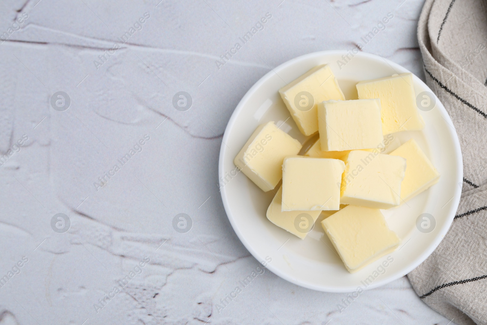 Photo of Pieces of fresh butter on white textured table, top view. Space for text