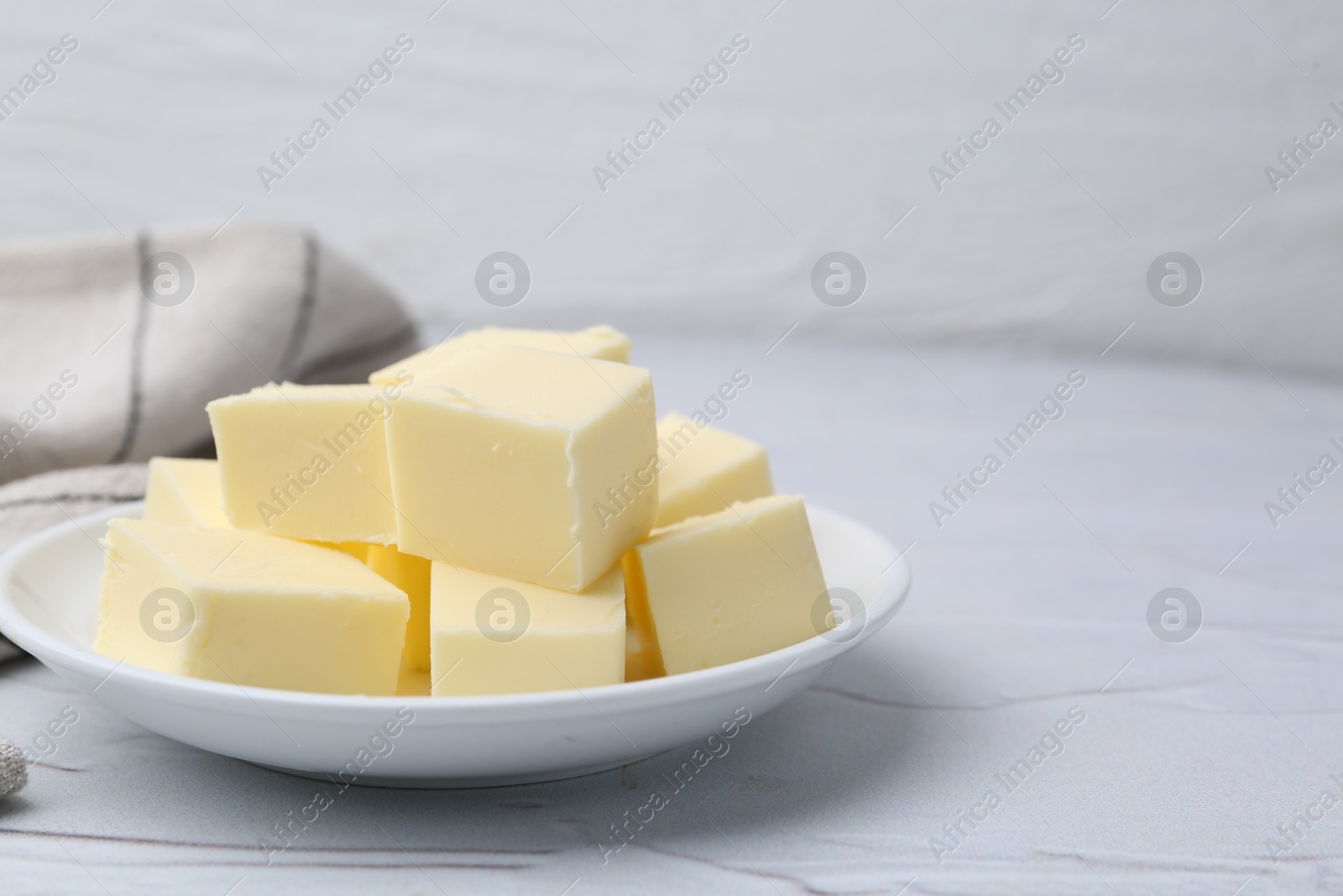 Photo of Pieces of fresh butter on white textured table, closeup. Space for text