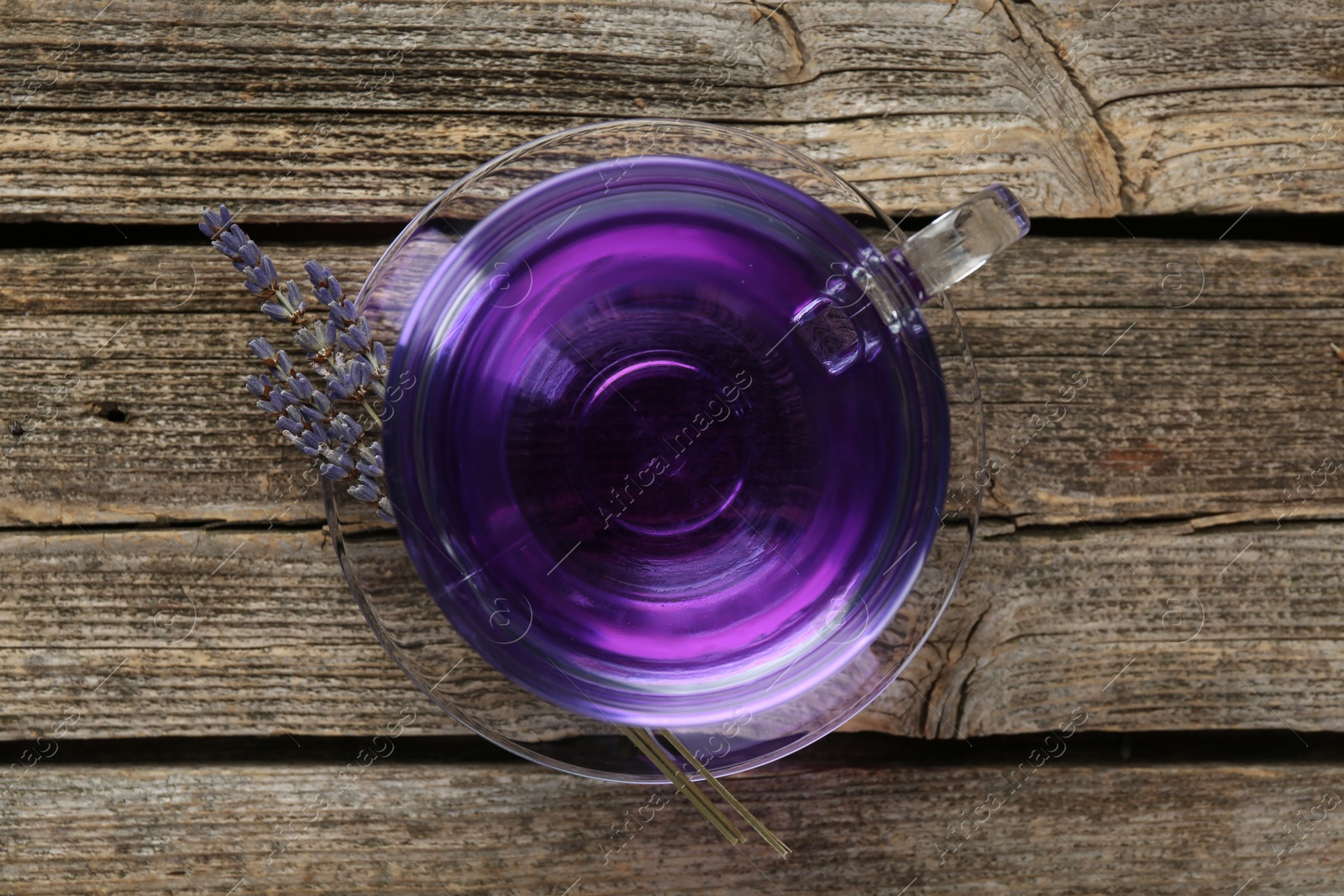 Photo of Aromatic lavender tea in glass cup and dry flowers on wooden table, top view