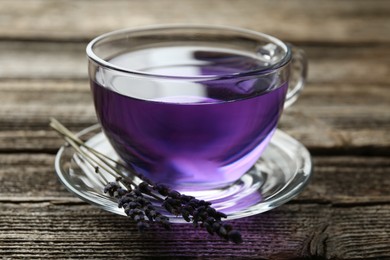 Photo of Aromatic lavender tea in glass cup and dry flowers on wooden table, closeup