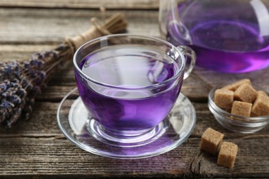 Aromatic lavender tea in glass cup, brown sugar and bunch of dry flowers on wooden table, closeup