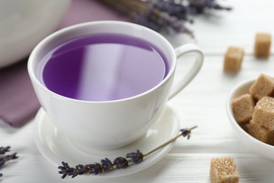 Aromatic lavender tea in cup, brown sugar and dry flowers on white wooden table, closeup