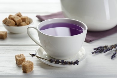 Aromatic lavender tea in cup, brown sugar and dry flowers on white wooden table, closeup