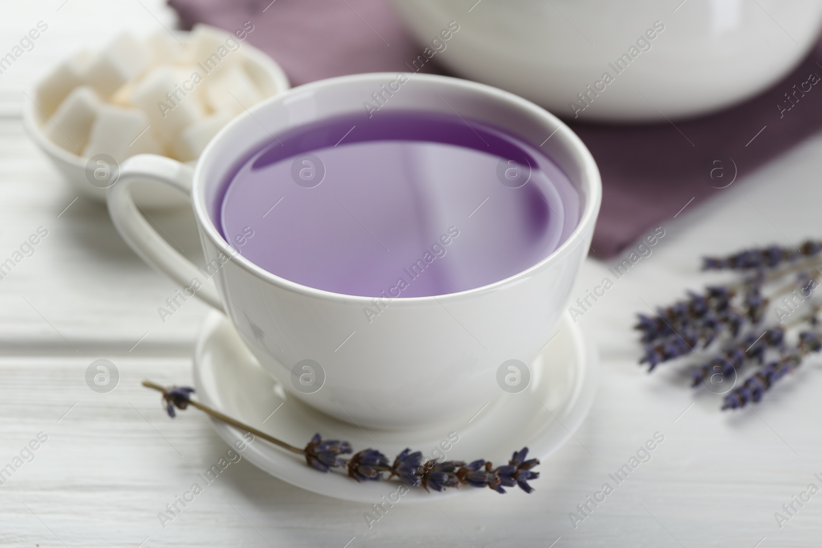 Photo of Aromatic lavender tea in cup, sugar cubes and dry flowers on white wooden table, closeup