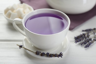 Aromatic lavender tea in cup, sugar cubes and dry flowers on white wooden table, closeup