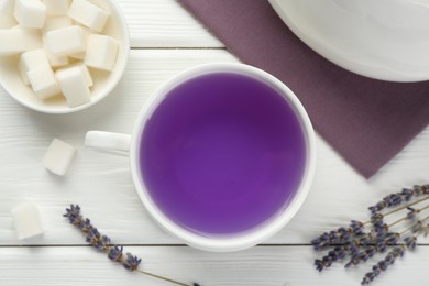 Aromatic lavender tea in cup, sugar cubes and dry flowers on white wooden table, flat lay