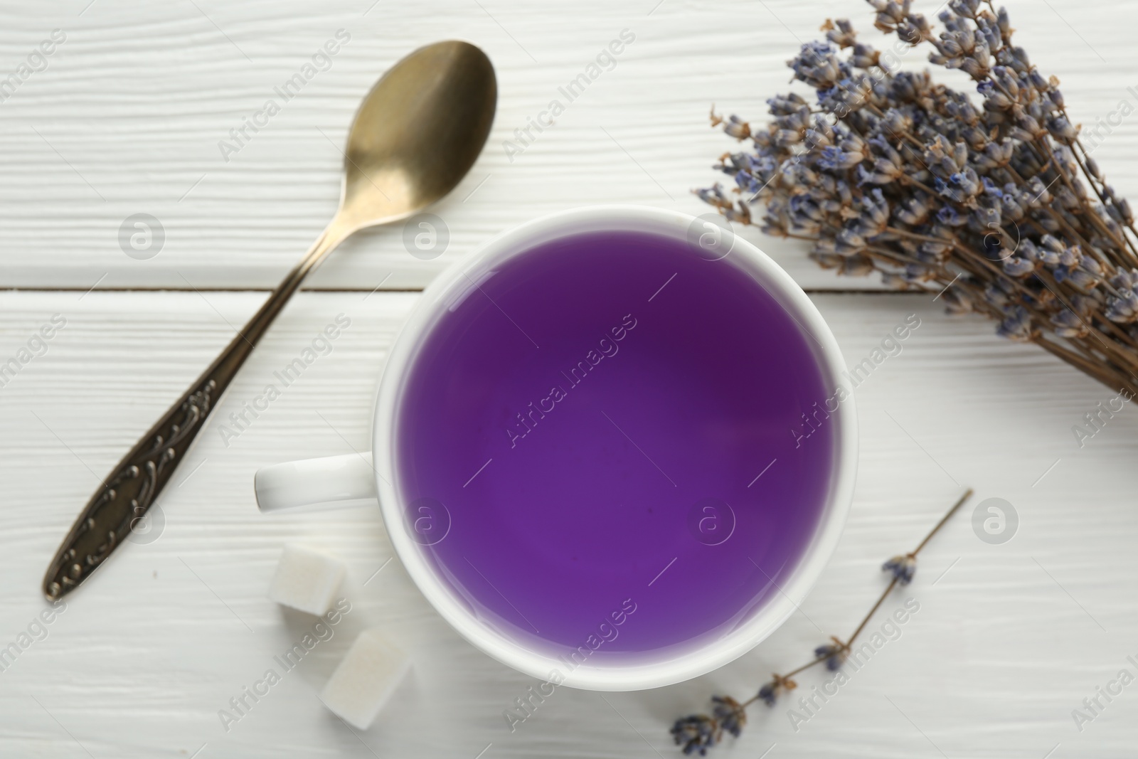 Photo of Aromatic lavender tea in cup, sugar cubes, spoon and bunch of dry flowers on white wooden table, flat lay