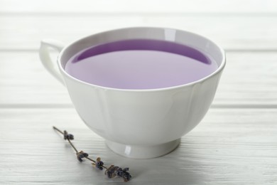 Aromatic lavender tea in cup and dry flowers on white wooden table, closeup