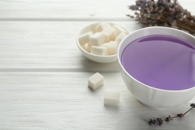 Aromatic lavender tea in cup, sugar cubes and dry flowers on white wooden table, closeup. Space for text