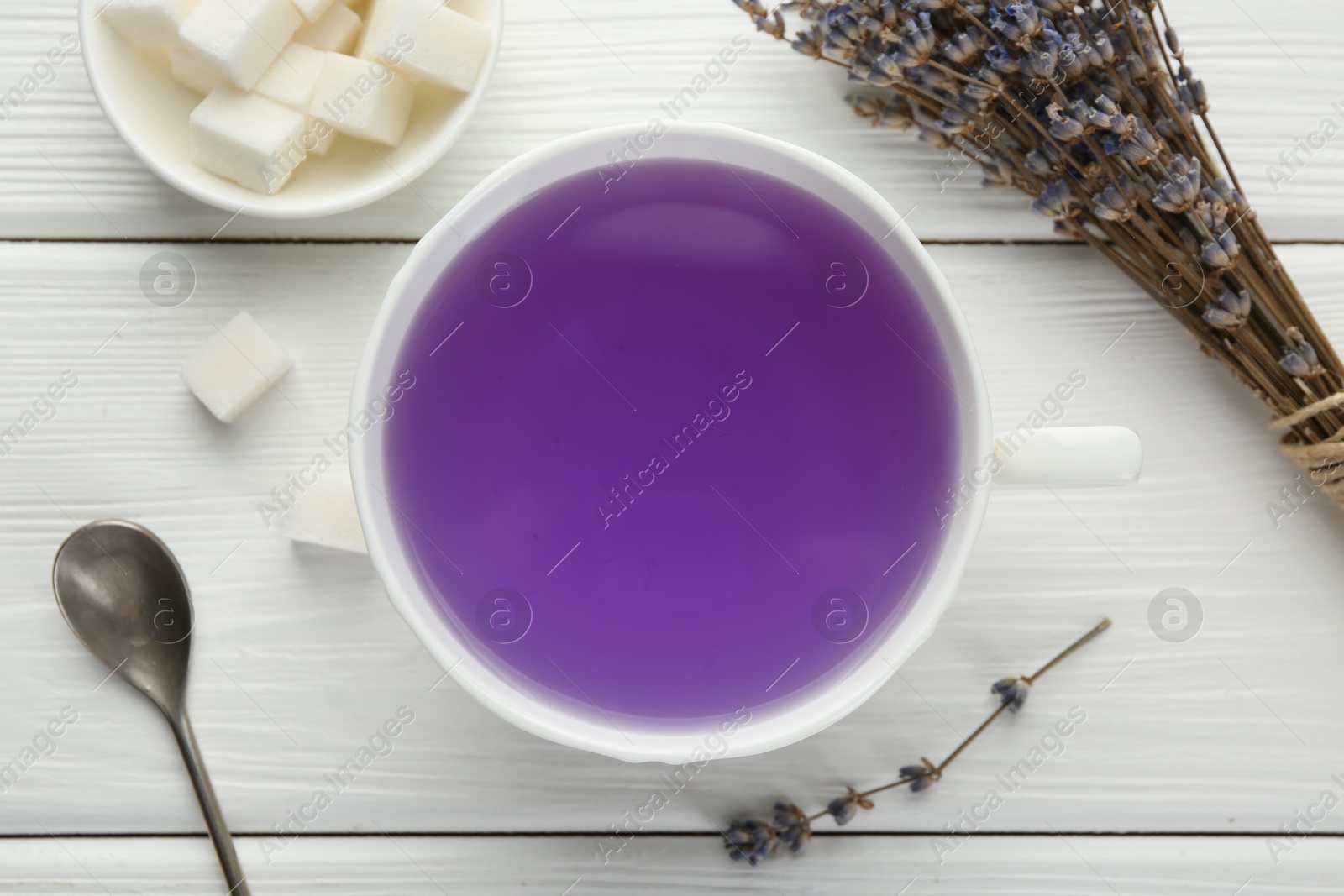 Photo of Aromatic lavender tea in cup, sugar cubes, spoon and bunch of dry flowers on white wooden table, flat lay