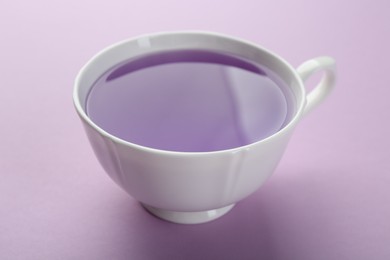 Aromatic lavender tea in cup on lilac background, closeup