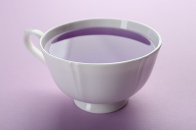 Aromatic lavender tea in cup on lilac background, closeup