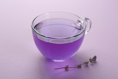 Photo of Aromatic lavender tea in cup and dry flowers on lilac background, closeup