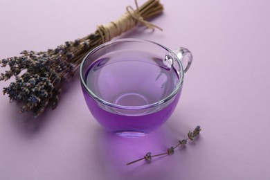 Aromatic lavender tea in glass cup and bunch of dry flowers on lilac background, closeup