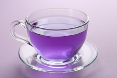 Aromatic lavender tea in cup on lilac background, closeup