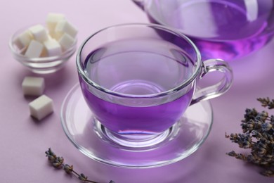 Photo of Aromatic lavender tea in glass cup, sugar cubes and dry flowers on lilac background, closeup