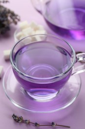 Aromatic lavender tea in glass cup and dry flowers on lilac background, closeup