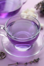 Aromatic lavender tea in glass cup and dry flowers on lilac background, closeup