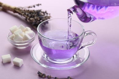 Pouring lavender tea into glass cup on lilac background, closeup