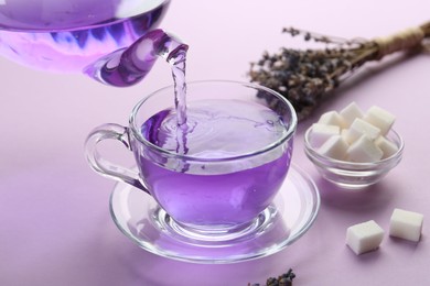 Pouring lavender tea into glass cup on lilac background, closeup