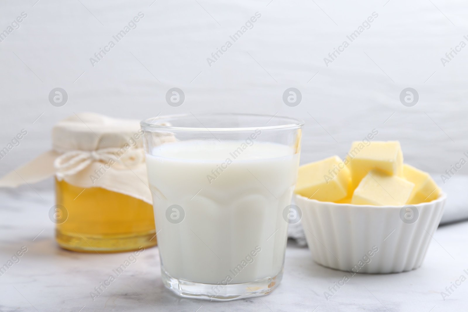 Photo of Fresh milk in glass, honey and butter on white marble table, closeup