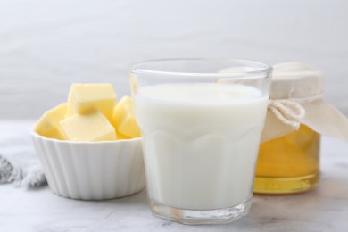 Fresh milk in glass, honey and butter on white marble table, closeup