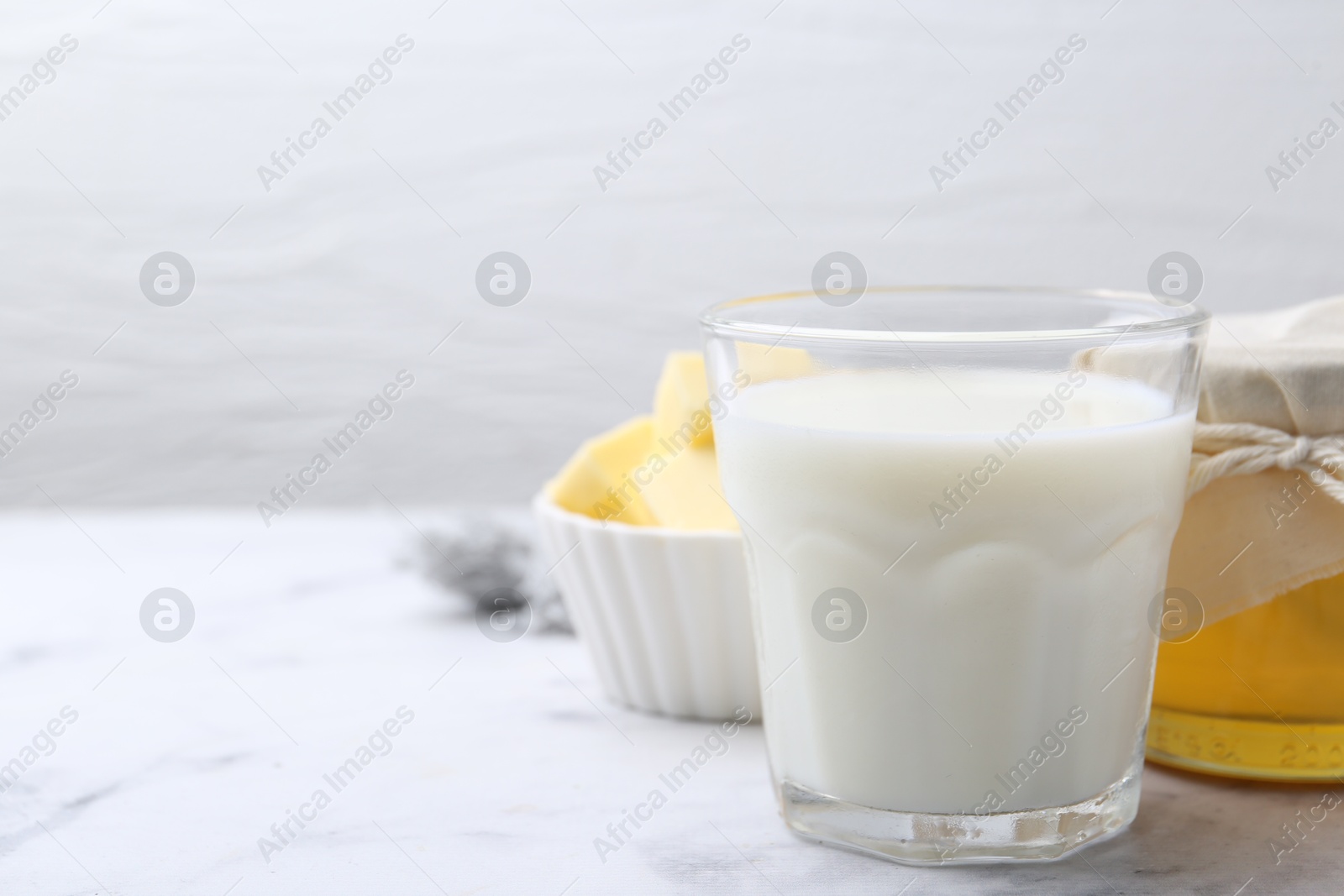 Photo of Fresh milk in glass, honey and butter on white marble table, closeup. Space for text