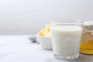 Fresh milk in glass, honey and butter on white marble table, closeup. Space for text