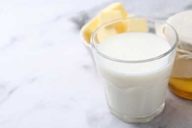 Fresh milk in glass, honey and butter on white marble table, closeup. Space for text