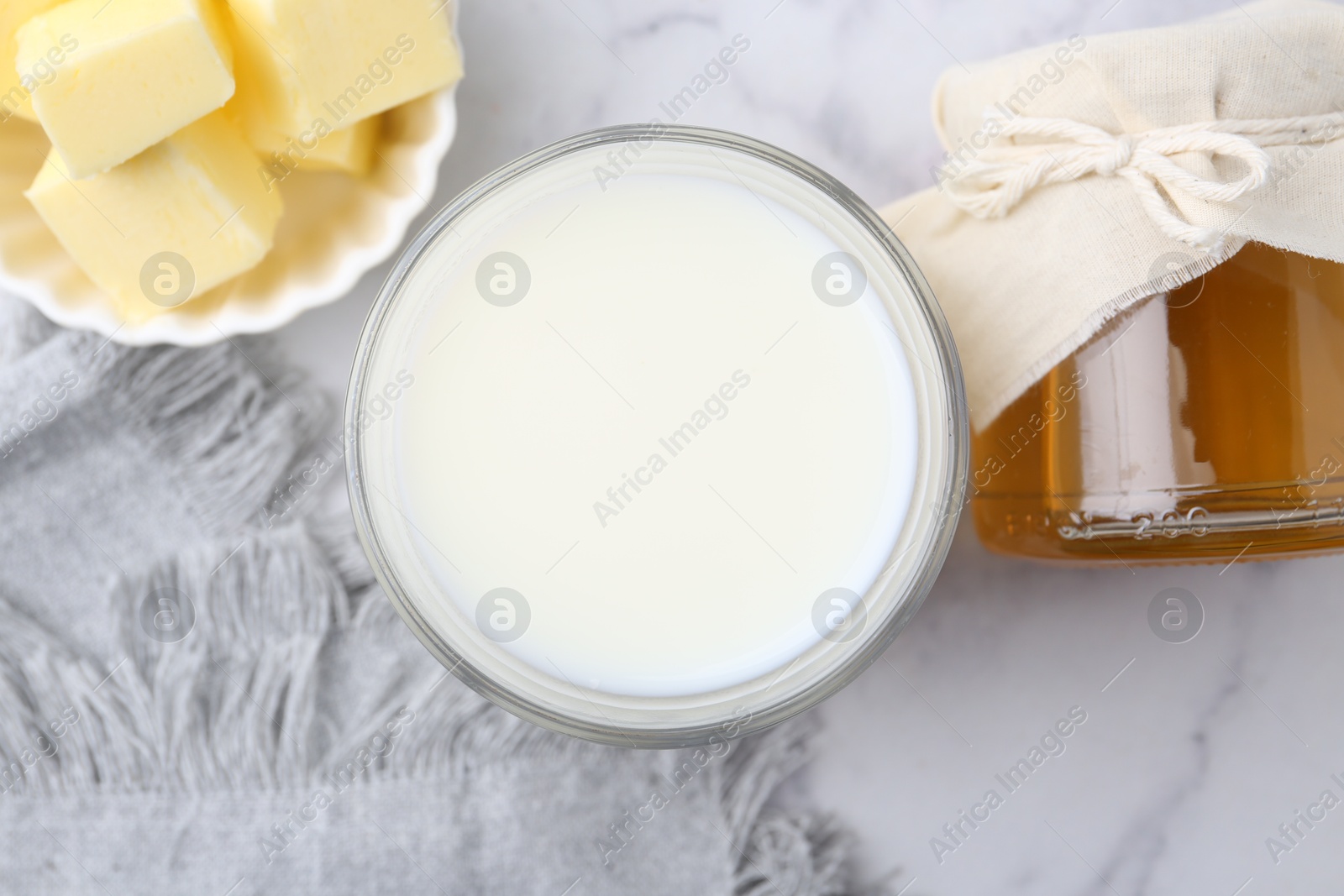 Photo of Fresh milk in glass, honey and butter on white marble table, flat lay