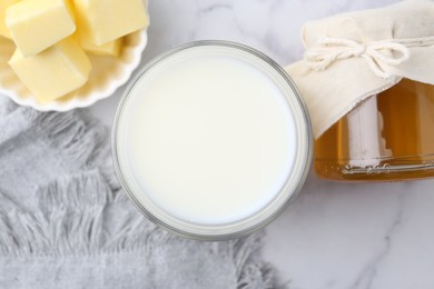 Fresh milk in glass, honey and butter on white marble table, flat lay