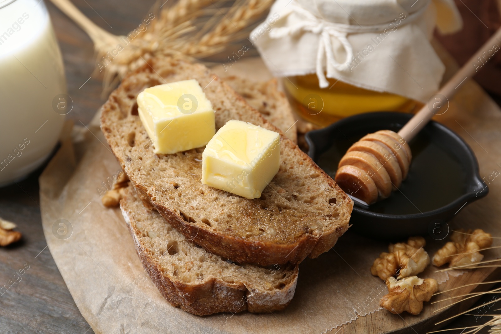 Photo of Slices of bread with butter, honey, milk and walnuts on wooden table, closeup